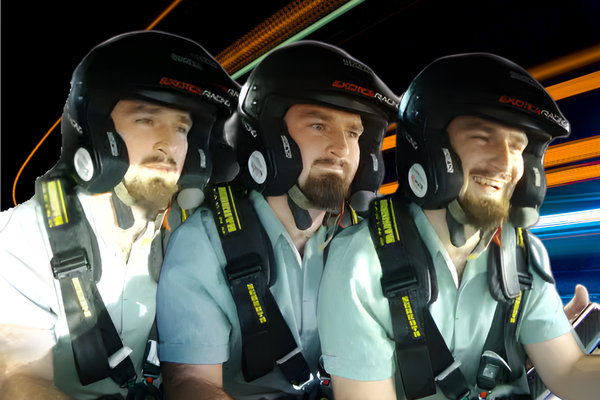 Three men wearing black racing helmets and multi-point safety harnesses ride in a high-performance vehicle, transitioning from focused expressions to visible excitement during a track experience.