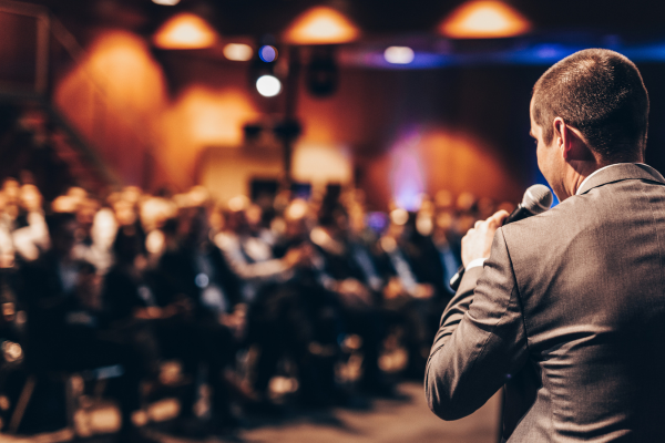 Speaker presenting at a travel industry conference with audience listening during a business event
