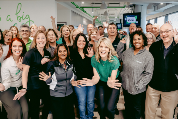Group of travel professionals smiling and waving in a collaborative office environment