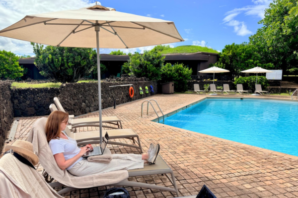 Woman working remotely on laptop by poolside, representing flexible travel agent lifestyle