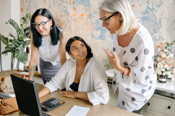 Three business professionals collaborating at a desk with a computer, discussing strategy and teamwork in a modern office setting.