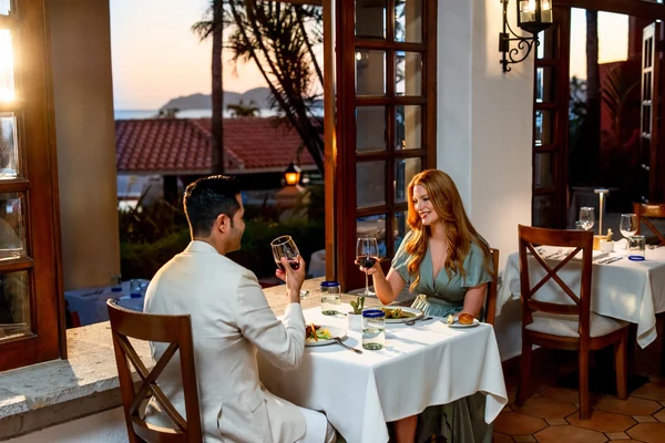 Couple enjoying evening dining with wine at Zoetry Casa del Mar Los Cabos overlooking the ocean at sunset