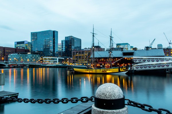 Boston Tea Party ship illuminated at twilight in Boston Harbor with the city skyline behind, a key revolutionary stop on the American Stories Travel multi-destination route