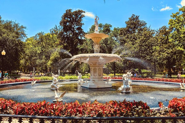 The iconic white Forsyth Park Fountain surrounded by red flowers and lush trees in Savannah, Georgia, completing the Southern leg of American Stories Travel's Lowcountry journey