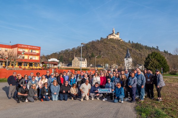 Large group of Dream Vacations franchise owners posing together with Marksburg Castle in the background during a Rhine River Dream Vacations event