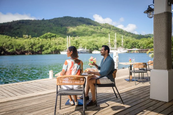 Couple enjoying cocktails at a waterfront dining table overlooking the marina and lush green hillside at Zoëtry Marigot Bay, St. Lucia