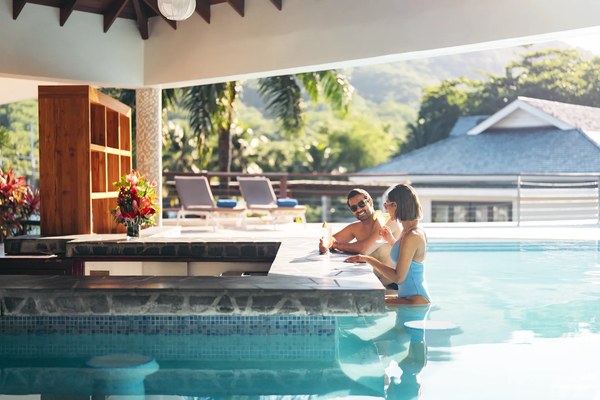 Couple enjoying drinks at the Le Bateau swim-up pool bar at Zoëtry Marigot Bay, St. Lucia, with mountains in the background
