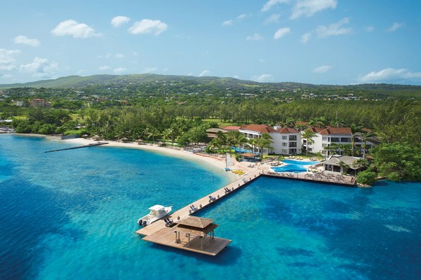 Aerial view of Zoëtry Montego Bay Jamaica showing the private beach, wooden pier, white buildings with red-tile roofs, and the Rose Hall hillside