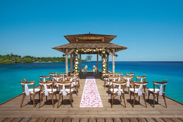 Wedding ceremony setup with floral gazebo, white chairs, and rose petal aisle on the dock over the turquoise sea at Zoëtry Montego Bay