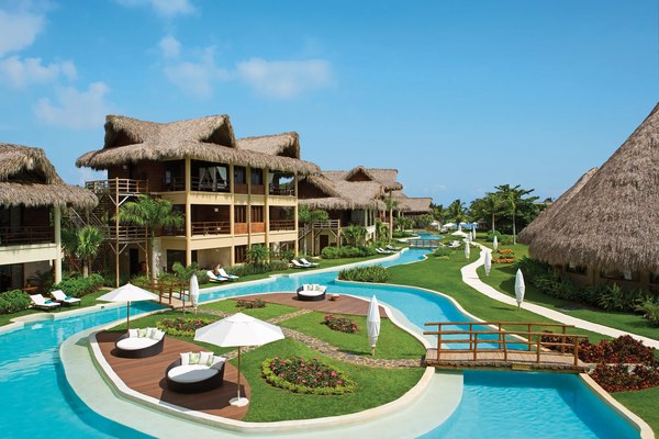 Lazy river pool winding through thatched-roof villas with private daybeds and umbrellas at Zoëtry Agua Punta Cana