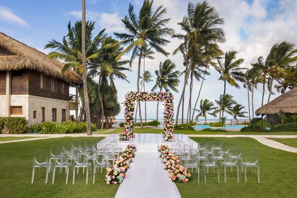 Beachside garden wedding setup at Zoëtry Agua Punta Cana with a floral arch, ghost chairs, and swaying palm trees