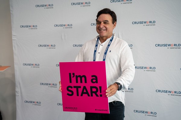 A travel advisor smiling and holding a pink I'm a STAR! sign in front of a CruiseWorld by Northstar backdrop