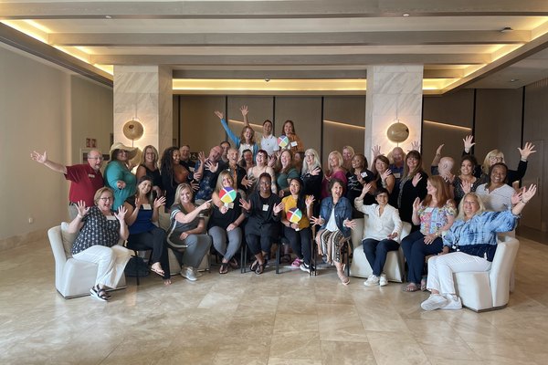 A large group of Nexion Travel Group advisors smiling, waving, and celebrating together at a community gathering