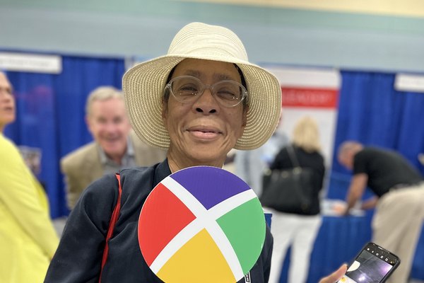 A Nexion Travel Group advisor smiling and holding the colorful Nexion X paddle on the show floor at a national travel convention