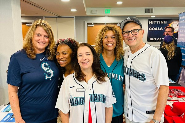 Travel advisors and a supplier partner wearing Seattle Mariners jerseys and connecting at a Travel Leaders Network trade show booth