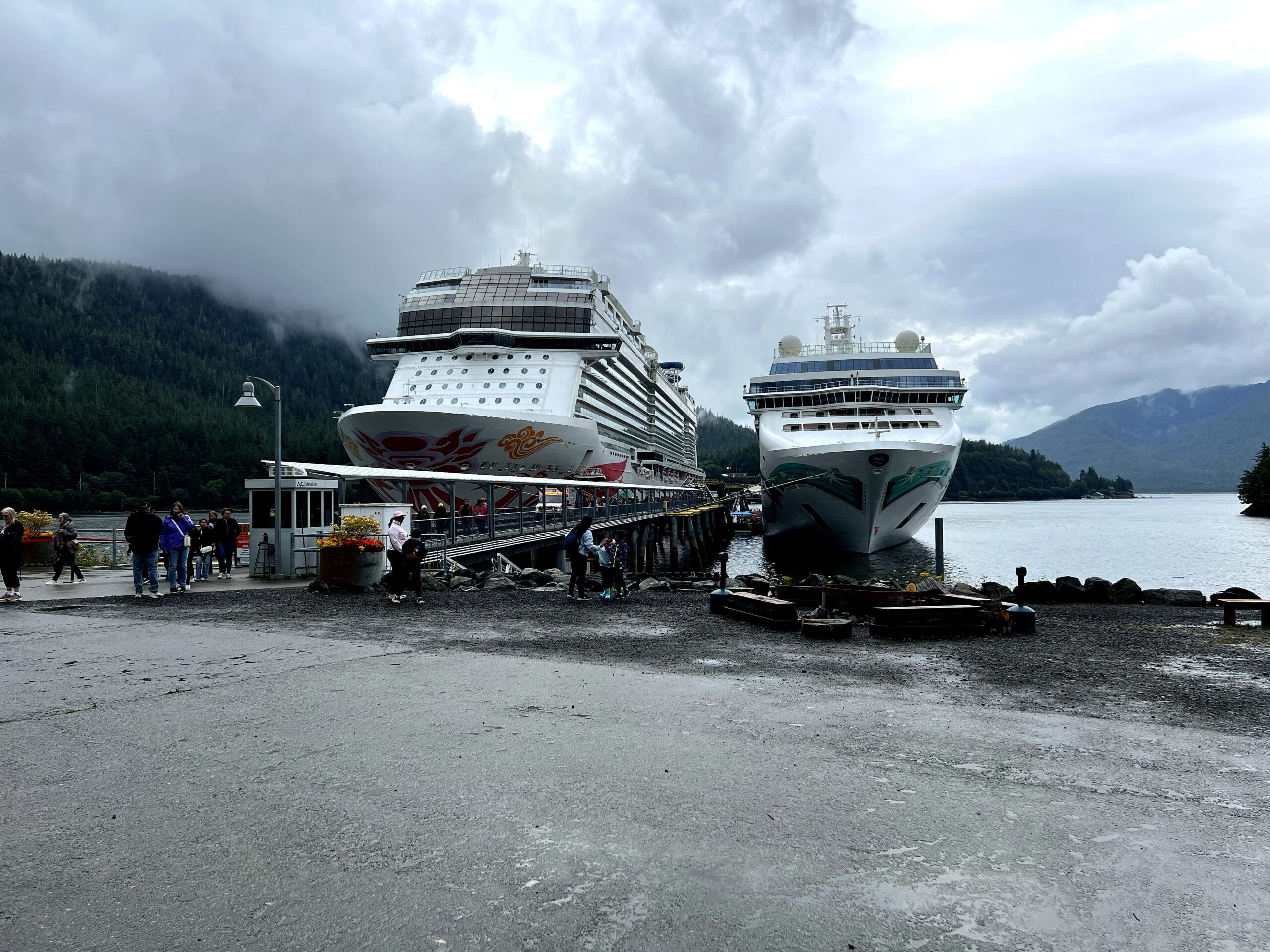 Norwegian Joy docked in Alaska alongside another cruise ship, with forested mountains in the background - Alaska Aboard the Norwegian Joy Review - Travel Professional NEWS